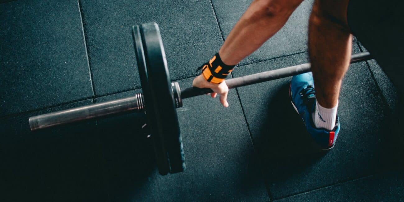 person wearing black shorts and blue lace up low top sneaker holding black barbell