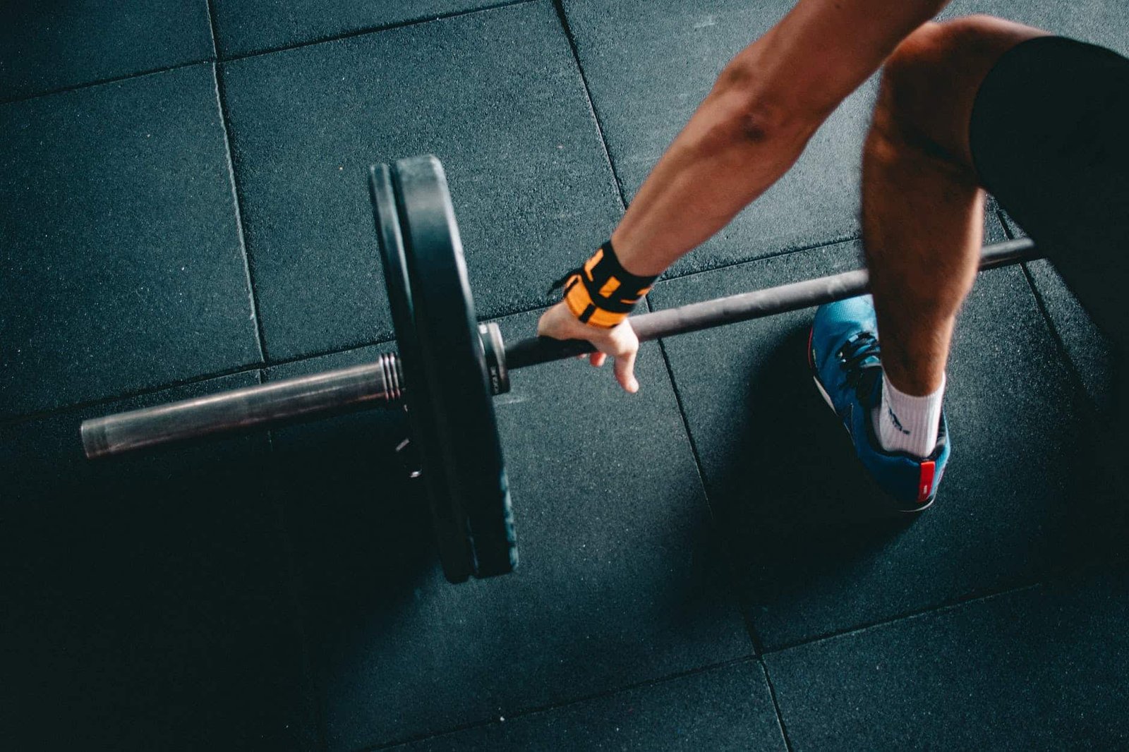 person wearing black shorts and blue lace up low top sneaker holding black barbell